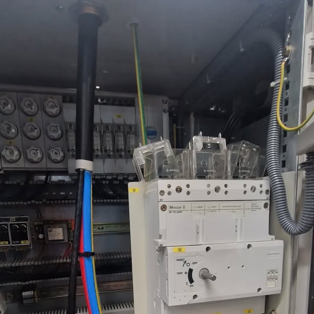 An open industrial control panel with a 400A switch-disconnector, shrouded fuse carriers and protective devices on a DIN rail