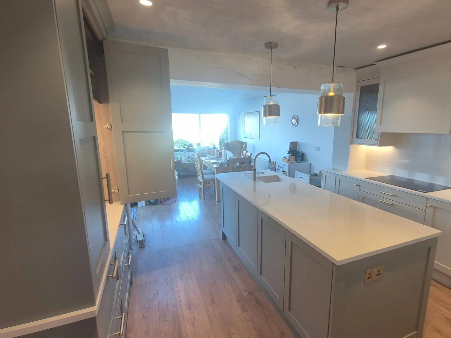 A finished kitchen with two glass pendant lights over the island, recessed ceiling downlights and under-cabinet lighting
